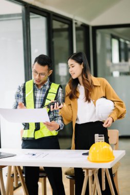 Mühendis takımı buluşması, birlikte çalışmak, mimari proje sahasında işçi yelekleri giymek ve model ev yapmak. Modern ofiste Asya endüstrisi profesyonel takımı
