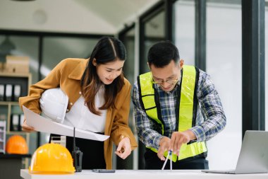 Mühendis takımı buluşması, birlikte çalışmak, mimari proje sahasında işçi yelekleri giymek ve model ev yapmak. Modern ofiste Asya endüstrisi profesyonel takımı