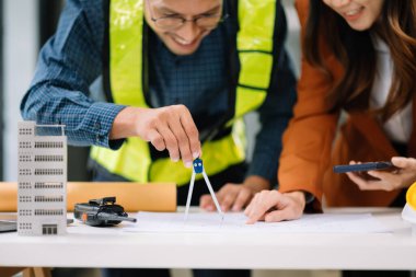 İki meslektaş verileri tartışıyor, inşaat ofisinde mimari proje üzerinde çalışıyor.