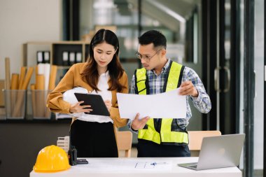 Mühendis takımı buluşması, birlikte çalışmak, mimari proje sahasında işçi yelekleri giymek ve model ev yapmak. Modern ofiste Asya endüstrisi profesyonel takımı