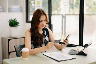 İş kadını akıllı telefon kullanıyor ve kredi kartını online alışveriş, omni kanalı, dijital tablet kenetleme klavye bilgisayarını ofiste tutuyor.