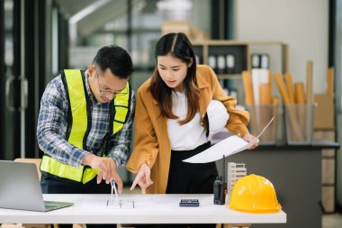 Mühendis takımı buluşması, birlikte çalışmak, mimari proje sahasında işçi yelekleri giymek ve model ev yapmak. Modern ofiste Asya endüstrisi profesyonel takımı