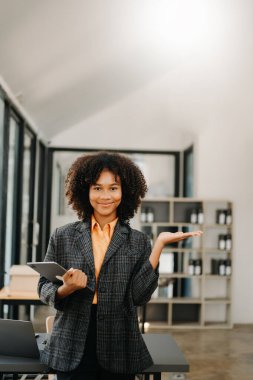 Kendine güvenen, gülümseyen, elinde tabletle modern ofiste duran Afrikalı kadın. 