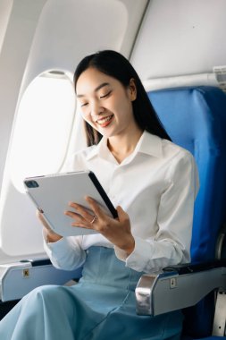 Çekici Asyalı kadın uçak yolcusu rahat koltukta dijital tabletle oturuyor. Stil olarak seyahat et