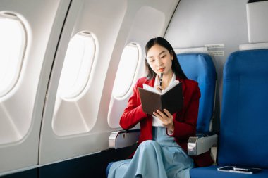 Çekici Asyalı kadın yolcu rahat koltukta otururken elinde not defteri tutuyor. Stil olarak seyahat et