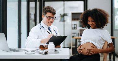 Hamile Afrikalı kadının klinikte doktorla randevusu var. Erkek sıhhiye uzmanı annesinin karnında bebeğini kontrol ediyor. Hamilelik, sağlık konsepti