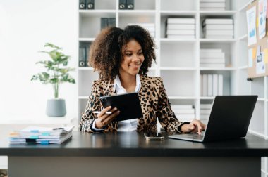 Genç Afrikalı kadın çalıştığı yerde dizüstü bilgisayar ve tablet kullanıyor. İşine odaklan.