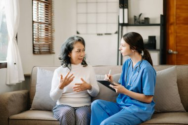 Genç doktor yaşlı kadınla ilgileniyor, dinliyor ve oturma odasında notlar alıyor.. 