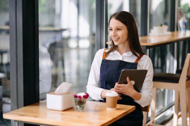 Elinde dijital tablet bulunan genç bayan kahveci kafede siparişleri almaya hazır.