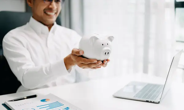 Asian Man are putting coins in a piggy bank for a business that grows for profit and saving money for the future. planning for retirement concept in office