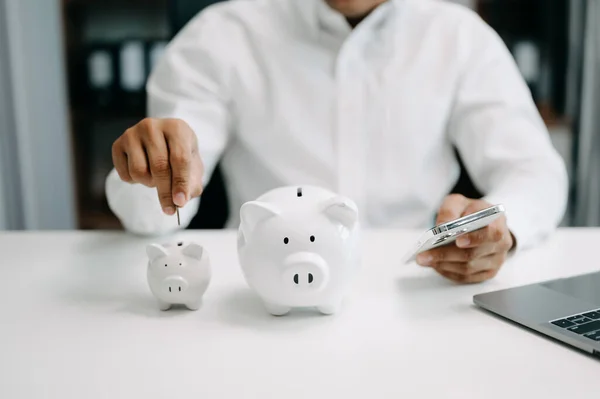Asian Man are putting coins in a piggy bank for a business that grows for profit and saving money for the future. planning for retirement concept in office