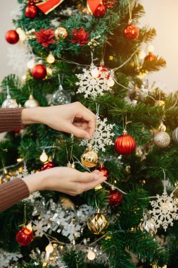 Kadın eli Noel ağacını oyuncaklarla süslüyor. Güneş ışığı odayı dolduruyor.