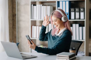 Genç Asyalı gülümseyen bir kadın elinde cep telefonuyla mesajlar yazıyor ya da haber yayınlarını okuyor, farklı oyunlar oynayıp eğlenmek için modern aletler kullanıyor.