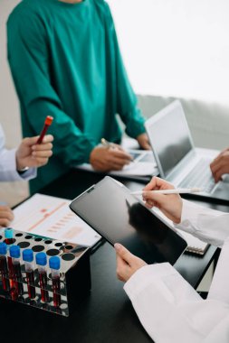Tıbbi ekip, beyaz önlüklü ve ameliyat önlüklü doktorlarla bir toplantı yapıyor. Masada oturmuş, tıp sektöründe çalışan bir hastayı tartışıyorlar. 