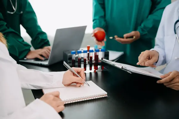 Medical team having a meeting with doctors in white lab coats and surgical scrubs seated at a table discussing a patients working in the medical industry
