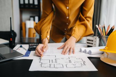 Kadın mimarın orta bölümü, masa başında mimari projeyle çalışıyor. 