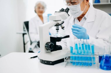 Bir tıp laboratuarında araştırma yapan kıdemli bilim adamları, ön plandaki bir araştırmacı tıp laboratuarında bir mikroskop kullanıyor.. 