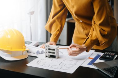 Kadın mimarın orta bölümü, masa başında mimari projeyle çalışıyor. 