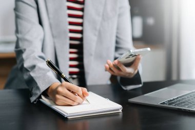Yeni modern dizüstü bilgisayarla çalışan iş kadını elleri ve akıllı telefondaki not defteri strateji diyagramına sabah ışığı altında yazılar.