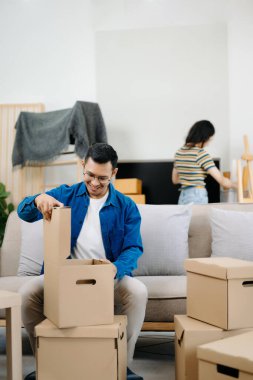 Asyalı genç ve çekici kadın ve erkek yeni eve karton paketle taşınıyorlar. Genç evli Asyalı eve taşınıyor.