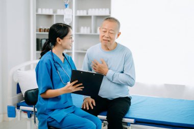 Asyalı doktor kıdemli hastayla konuşuyor ve hastane veya klinikte tuz çözeltisi alıyor.