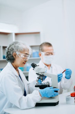 Bir tıp laboratuarında araştırma yapan kıdemli bilim adamları, ön plandaki bir araştırmacı tıp laboratuarında bir mikroskop kullanıyor.. 
