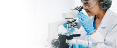 Bir tıp laboratuarında araştırma yapan kıdemli bilim adamları, ön plandaki bir araştırmacı tıp laboratuarında bir mikroskop kullanıyor.. 