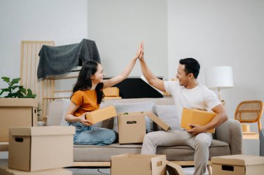 Asyalı genç ve çekici kadın ve erkek yeni eve karton paketle taşınıyorlar. Genç evli Asyalı eve taşınıyor.