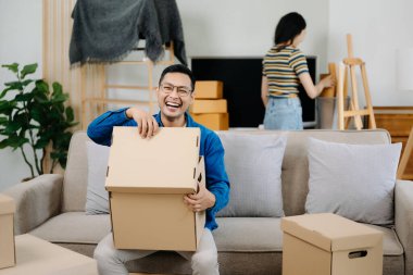 Asyalı genç ve çekici kadın ve erkek yeni eve karton paketle taşınıyorlar. Genç evli Asyalı eve taşınıyor.