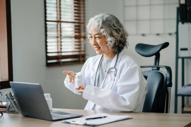 Asyalı gülümseyen doktor ya da danışman bir masada oturup dizüstü bilgisayarında görüntülü konuşma yapıyor.