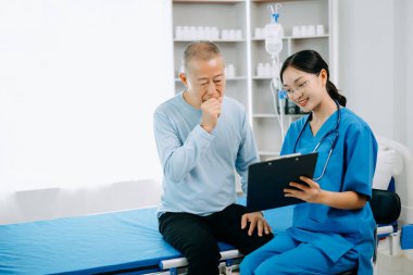 Asyalı doktor kıdemli hastayla konuşuyor ve hastane veya klinikte tuz çözeltisi alıyor.