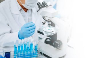 Bir tıp laboratuarında araştırma yapan kıdemli bilim adamları, ön plandaki bir araştırmacı tıp laboratuarında bir mikroskop kullanıyor.. 