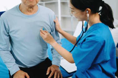 Asyalı doktor kıdemli hastayla konuşuyor ve hastane veya klinikte tuz çözeltisi alıyor.