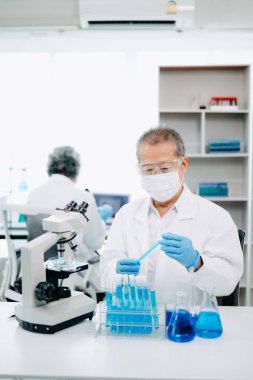 Bir tıp laboratuarında araştırma yapan kıdemli bilim adamları, ön plandaki bir araştırmacı tıp laboratuarında bir mikroskop kullanıyor.. 