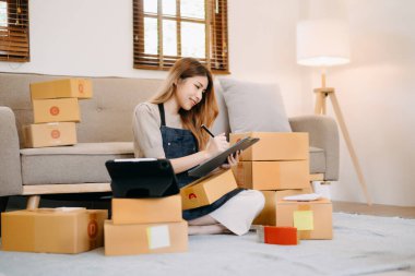 Genç bayan iş sahibi dizüstü bilgisayar kullanıyor ve evdeki müşterilere çevrimiçi siparişler göndermek için paketler hazırlıyor. Çevrimiçi Alışveriş kavramı