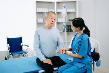 Asyalı doktor kıdemli hastayla konuşuyor ve hastane veya klinikte tuz çözeltisi alıyor.