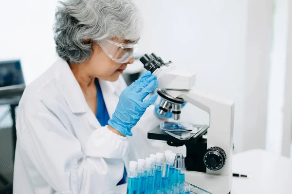 Senior scientists conducting research investigations in a medical laboratory, a researcher in the foreground is using a microscope in laboratory for medicine.