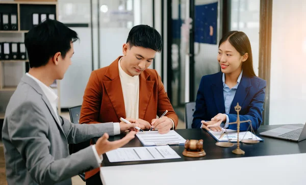 Asyalı iş adamları şefkatle el ele tutuşup, ofis odasında sözleşme belgelerini tartışıyorlar.