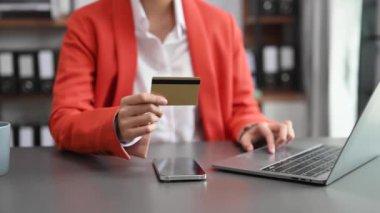 İş kadını elleri dizüstü bilgisayar kullanıyor ve ofiste kredi kartı tutuyor.  