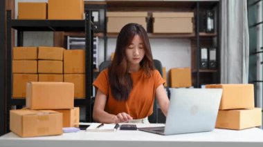 Genç işyeri sahibi kadın paket kutusu hazırlıyor ve online alışveriş konsepti üzerinde müşteriye teslim edilmesi için online olarak kontrol ediliyor..