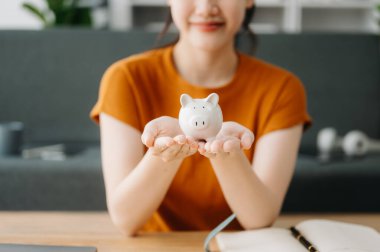 Asyalı kadınların elleri hesaplamak için kumbaraya bozuk para atıyor. İş, finans, tasarruf ve emlak yatırım kavramı