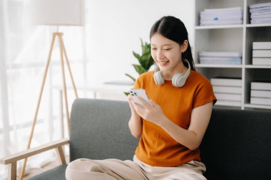 Asyalı kadın evdeki kanepede akıllı telefon kullanıyor.