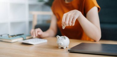 Asyalı kadınların elleri hesaplamak için kumbaraya bozuk para atıyor. İş, finans, tasarruf ve emlak yatırım kavramı