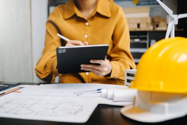 Kadın mimarın orta bölümü, masa başında mimari projeyle çalışıyor. 