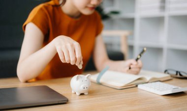 Asyalı kadınların elleri hesaplamak için kumbaraya bozuk para atıyor. İş, finans, tasarruf ve emlak yatırım kavramı