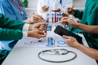 Tıbbi ekip, beyaz laboratuvar önlüklü ve ameliyat önlüklü doktorlarla bir toplantı yapıyor. Masada oturmuş, tıp endüstrisinde tablet kullanan hastaları tartışıyorlar.