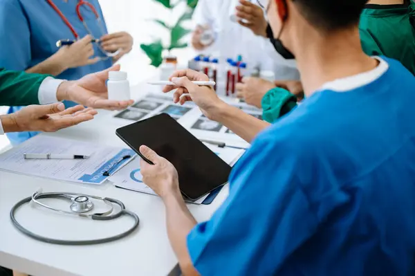 Medical team having a meeting with doctors in white lab coats and surgical scrubs seated at a table discussing a patients working online using  tablet in the medical industry