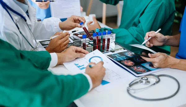 Medical team having a meeting with doctors in white lab coats and surgical scrubs seated at a table discussing a patients working online using  tablet in the medical industry