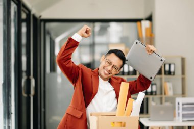 Mutlu ve heyecanlı Asyalı genç ofis çalışanı istifasını kutluyor, kişisel eşyalarını taşıyor. Modern ofisteki işi bırakmak, değiştirmek ya da şirket kurmak