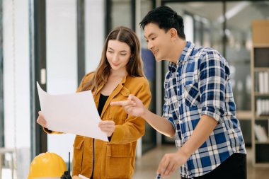 Two colleagues discussing data working with architectural project at construction site at desk in office